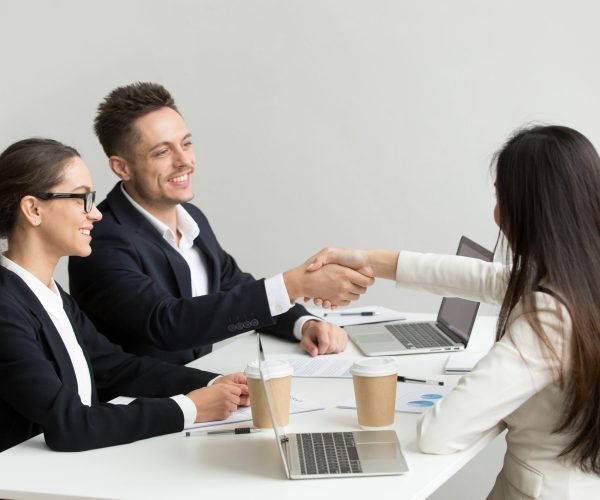 Friendly satisfied partners handshaking at group meeting thanking for successful teamwork, smiling millennial businessman shaking hand greeting businesswoman, respect or making contract deal concept